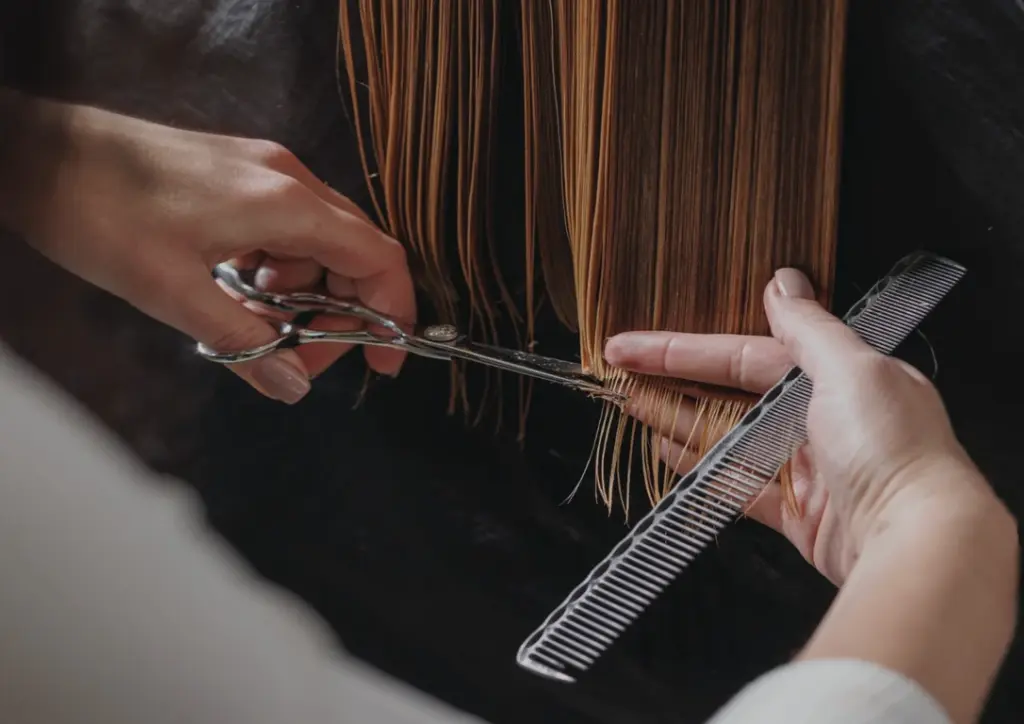 Professional hair stylist cutting straight blonde hair with salon shears and a comb during a haircut appointment